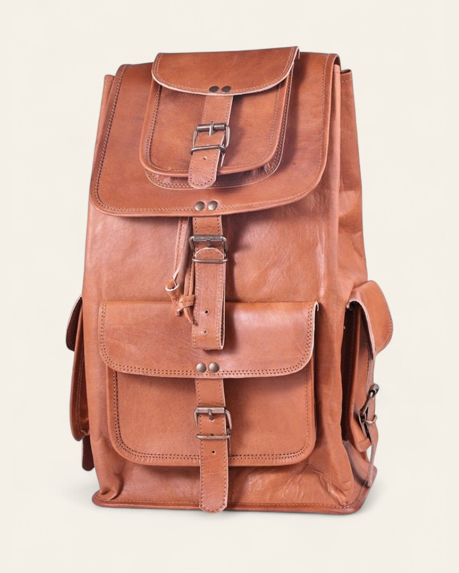 The Aravalli Backpack — handcrafted tan real leather rucksack with buckled top flap and three exterior pockets, front view
