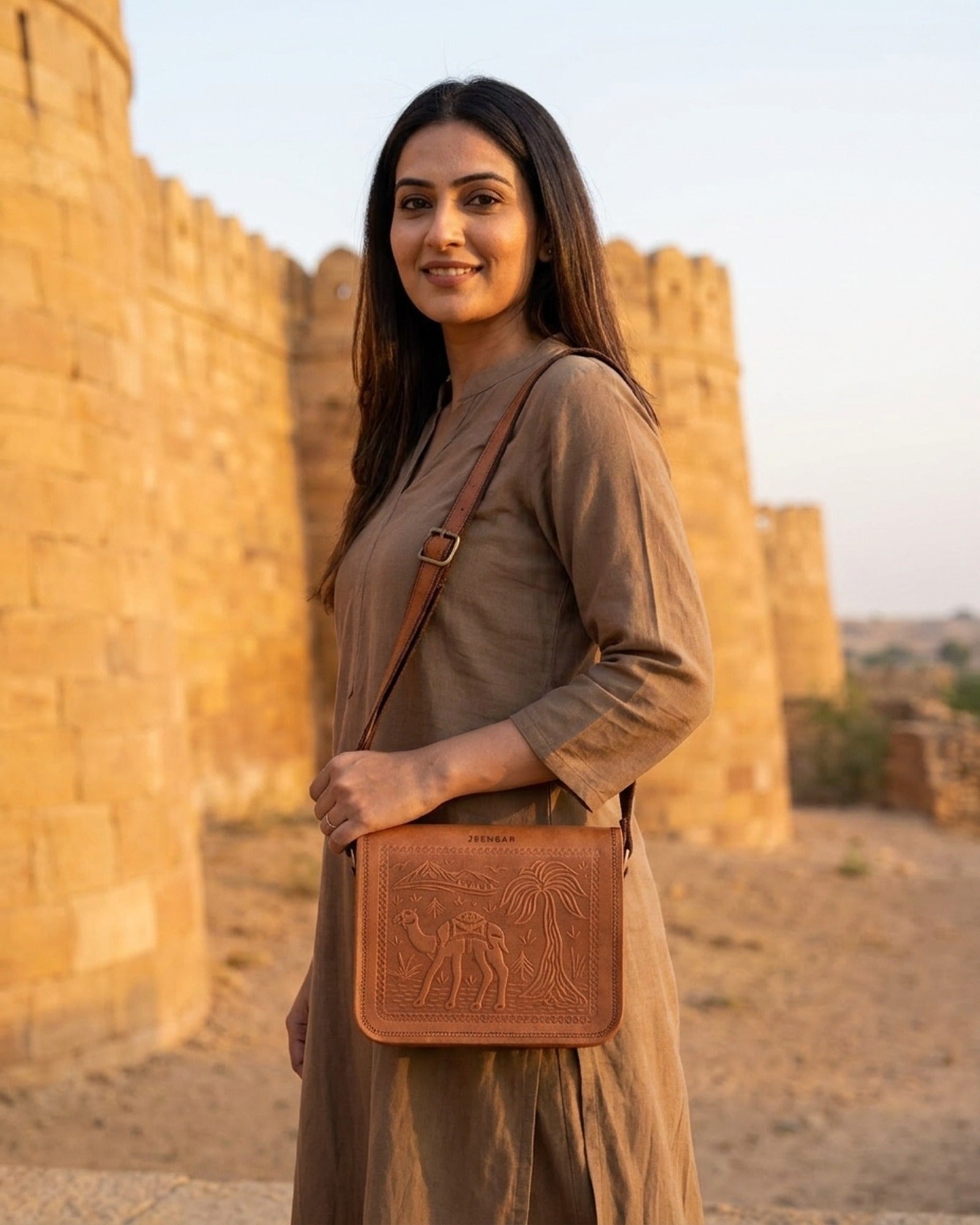 The Jaisalmer Sling in Tan worn crossbody against a golden sandstone fort wall