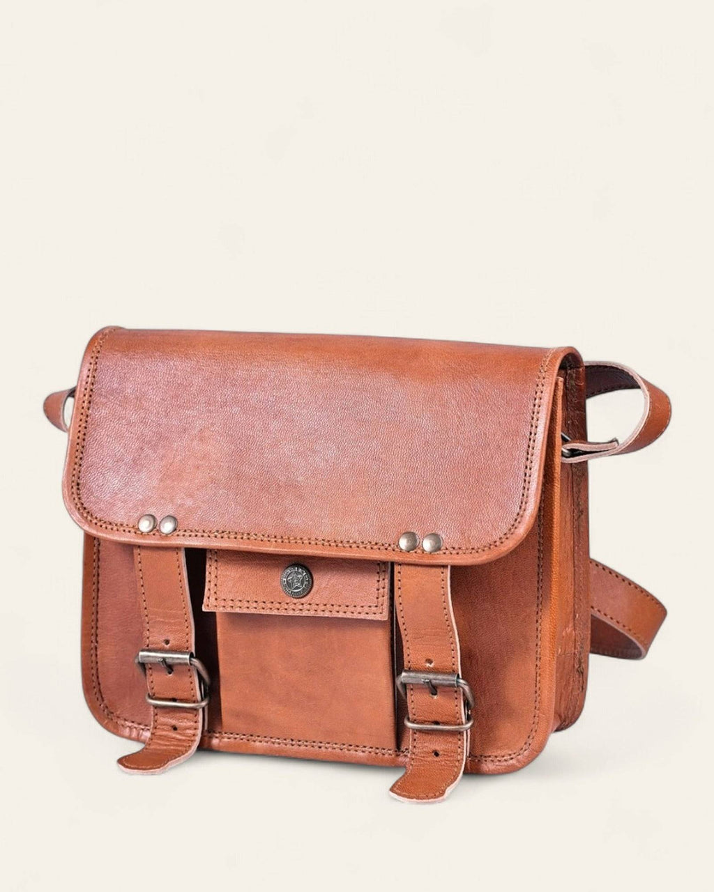 The Jaigarh Sling in natural certified leather, front view with twin buckle straps and antique-brass concho